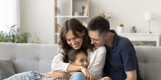 Happy young parents cuddling their daughter on the living-room couch, illustrating how avoiding Covered California enrollment mistakes helps protect their family’s health coverage