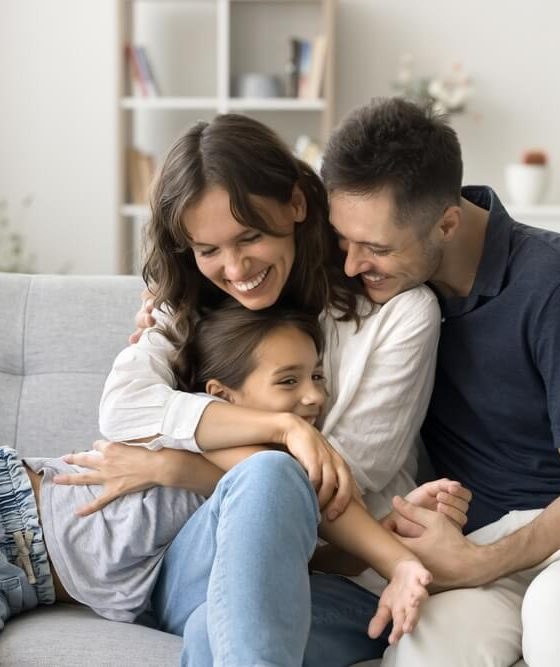 Happy young parents cuddling their daughter on the living-room couch, illustrating how avoiding Covered California enrollment mistakes helps protect their family’s health coverage