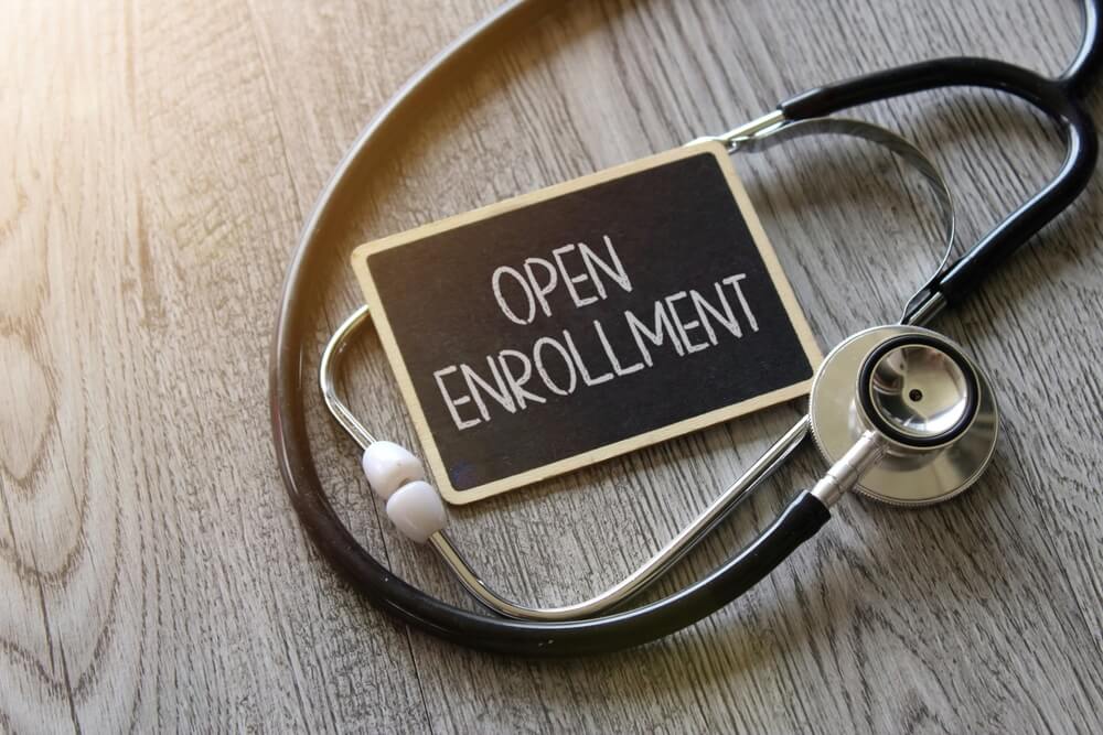 Stethoscope beside a chalkboard reading OPEN ENROLLMENT on a wooden table, highlighting the importance of avoiding Covered California enrollment mistakes