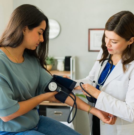 Medical provider takes blood pressure of female patient.
