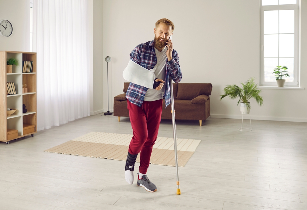 Man with broken leg on crutches talks on phone to his provider about his Covered California 2026 benefits.