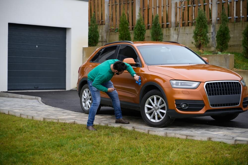 Man inspecting a dented car parked in a residential driveway, representing scenarios where homeowners insurance may cover driveway damage