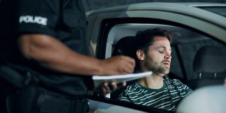 Police officer speaking with a driver sitting in his car after a crash, documenting details for insurance after an accident.