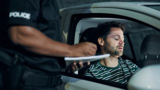 Police officer speaking with a driver sitting in his car after a crash, documenting details for insurance after an accident.