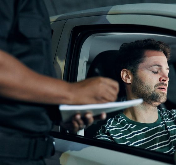 Police officer speaking with a driver sitting in his car after a crash, documenting details for insurance after an accident.