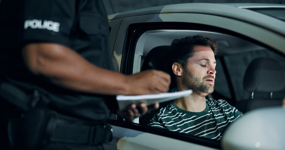 Police officer speaking with a driver sitting in his car after a crash, documenting details for insurance after an accident.