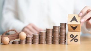 Rising stacks of coins beside a toy car and blocks with arrows and a percent symbol representing why car insurance rates change, including factors like inflation, accident claims, repair costs, driver risk, and insurance market trends.
