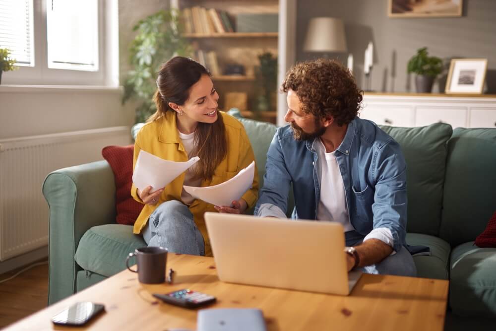 Couple reviewing bills and documents at home with a laptop, preparing for a spring home insurance review to update coverage.