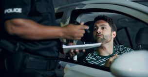 Police officer issues a ticket to a worried driver during a traffic stop, illustrating what happens if insurance lapses.