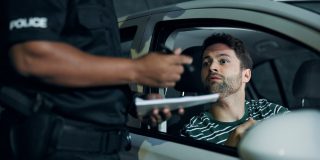 Police officer issues a ticket to a worried driver during a traffic stop, illustrating what happens if insurance lapses.