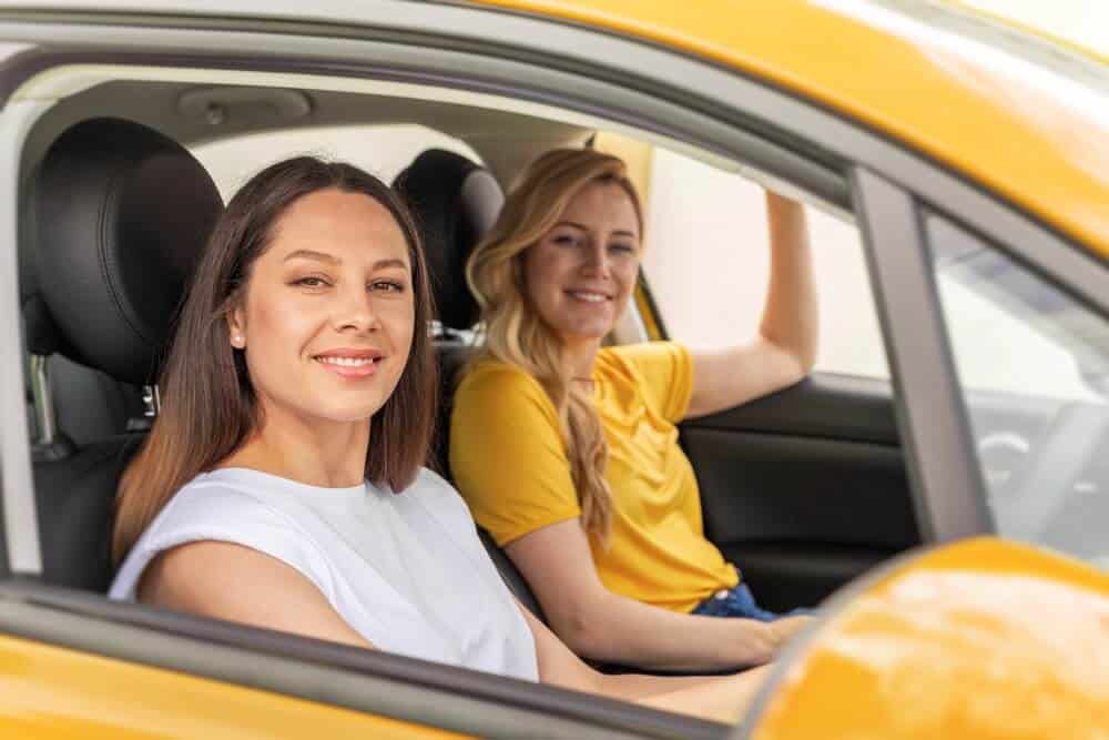 Two women ride in a yellow car, illustrating safe car-sharing habits and permissive driving coverage in everyday situations.