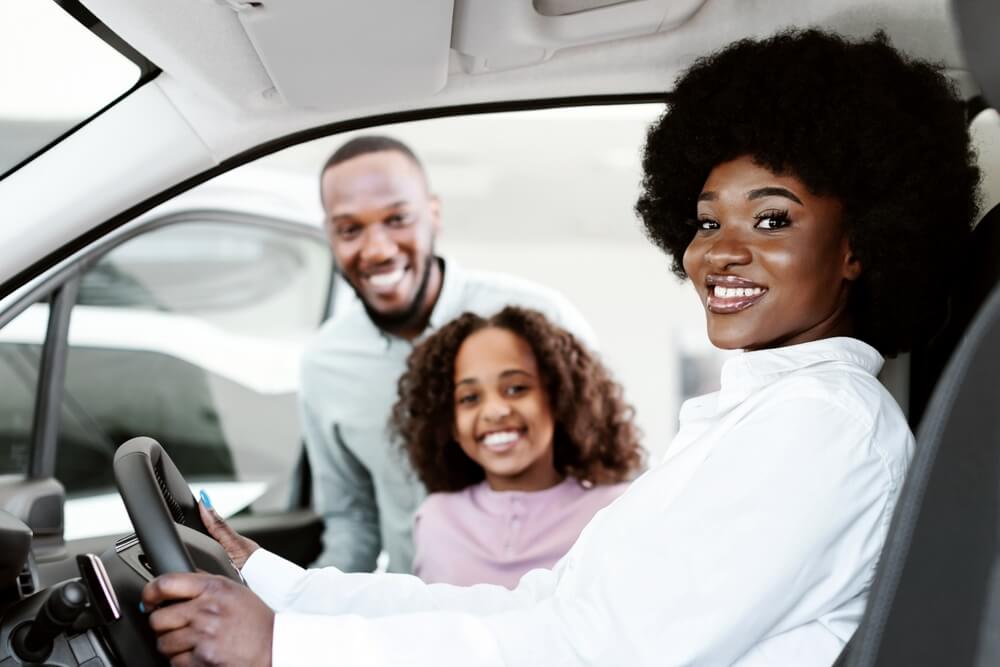 Smiling driver poses in a car while a father and child look on from the back seat, highlighting permissive driving.