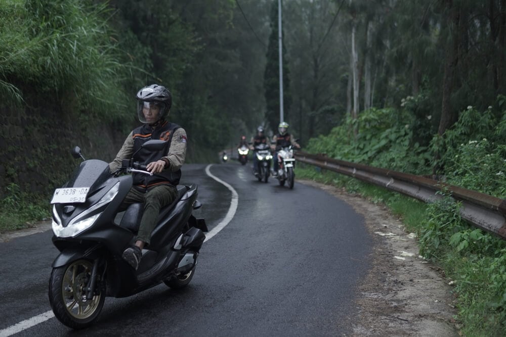 Rider on a scooter leads a group of motorcyclists along a winding, wet forest road, highlighting motorcycle insurance protecting riders on every trip.