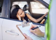 Officer writes a citation while a driver waits in her car, showing another example of the 5 common traffic violations that raise insurance rates.