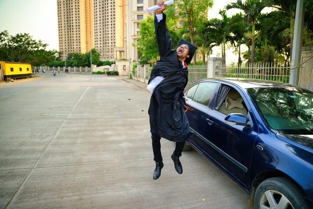 Recent graduate celebrating beside a car, representing life changes that make a June insurance review a smart time to update coverage.