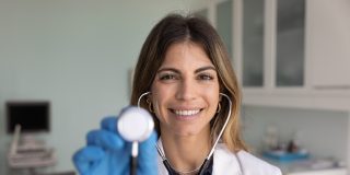 Preventative health care provider holding a stethoscope in a medical exam room during a routine wellness check.