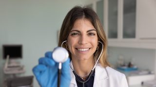 Preventative health care provider holding a stethoscope in a medical exam room during a routine wellness check.