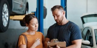 Customer and mechanic review a repair estimate on a clipboard inside an auto shop, showing why car repairs cost more than ever.