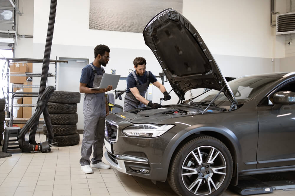 Two mechanics inspect a car engine with the hood open while reviewing diagnostics, showing why car repairs cost more than ever.