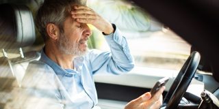 Worried driver checks his phone after a missed payment while sitting in his car.