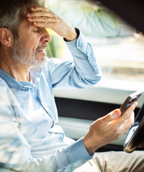 Worried driver checks his phone after a missed payment while sitting in his car.
