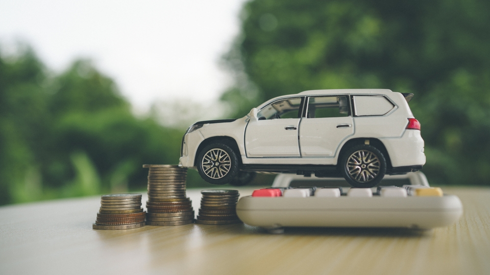 Model SUV displayed on a calculator beside stacks of coins, representing car insurance rates, vehicle costs, and premium calculations.