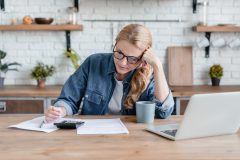 Woman reviewing insurance documents with a calculator and laptop at home.