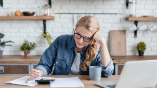Woman reviewing insurance documents with a calculator and laptop at home.