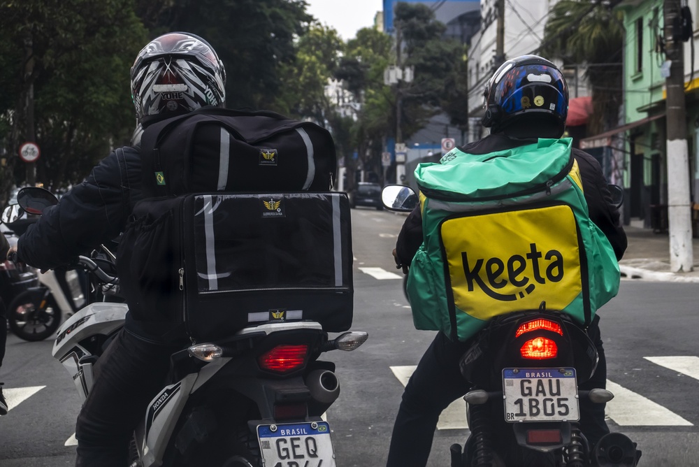 Gig delivery drivers on motorcycles riding through a city street.