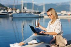 Freelancer working on a laptop while researching business insurance by a marina.