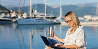 Freelancer working on a laptop while researching business insurance by a marina.