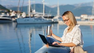 Freelancer working on a laptop while researching business insurance by a marina.