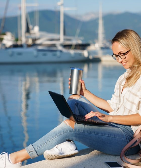 Freelancer working on a laptop while researching business insurance by a marina.