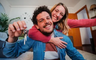 Young Caucasian couple showing keys of their first house after purchase and moving to new home together.