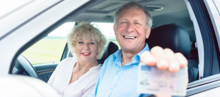 Portrait of a happy senior man showing his available driving license while sitting in the car next to his cheerful wife