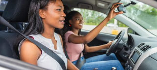 A Young black teenage driver seated in her new car with her mother