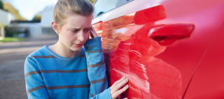 Young Worried Teenage Female Driver Looking at Damaged Car After Accident