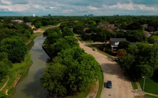 An aerial drone photo of a sunny summer day in Plano Texas next to a river park with a car driving on the street.