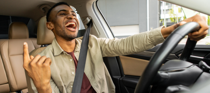 Joyful black man dancing in car, singing while driving his car. Road fun