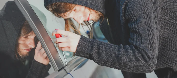 Anti theft system problem concept. Theft man dressed in black holding screwdriver trying to break into car.
