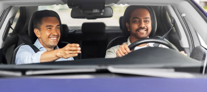 driver courses and people concept - happy smiling car driving school instructor teaching young man to drive.
