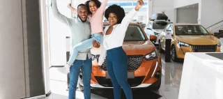 Full length of excited African American family lifting hands up, celebrating new car purchase at auto dealership – cheap car insurance.