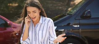 Stressed woman talking on phone after car accident outdoors – cheap car insurance.