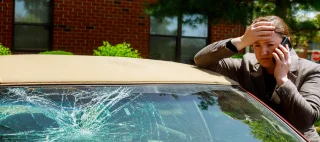 Woman making a phone call next to damaged car.