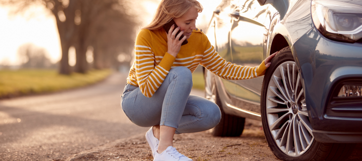 Woman Calling For Help On Phone After Car Breakdown On Country Road With Tire Puncture.