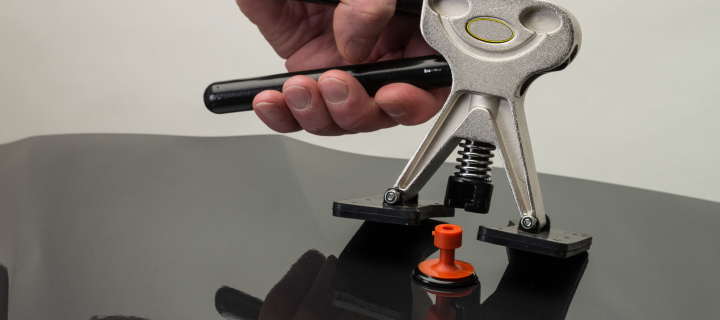 Man’s hand using a tool to perform paintless dent repair on a grey car.