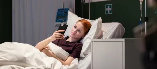 Red-haired patient enjoys a video call with someone, lying in the hospital bed.