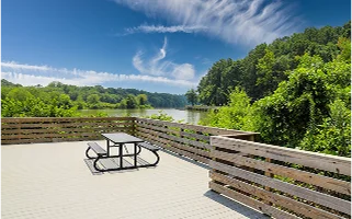 A long winding boardwalk along the Chattahoochee river with a wooden rail, still river water, green trees with blue sky and clouds at Roswell Riverwalk Boardwalk in Roswell Georgia – Roswell, cheap car insurance in Georgia