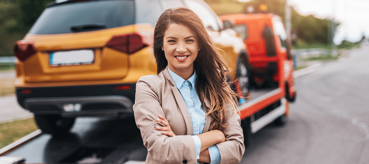 Woman standing in front of her car which is getting tolled by a crane