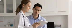 A female doctor showing information on a digital tablet to a man in a medical office.